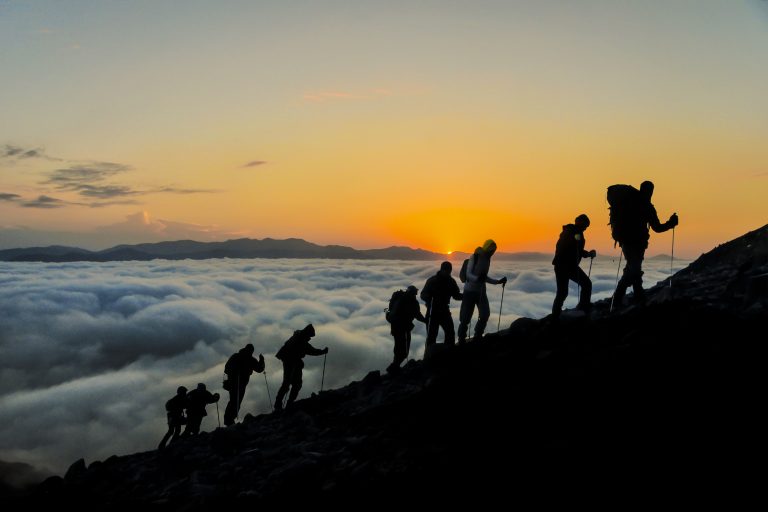 Silhouetten von Bergsteigern, die einen Gipfel erklimmen
